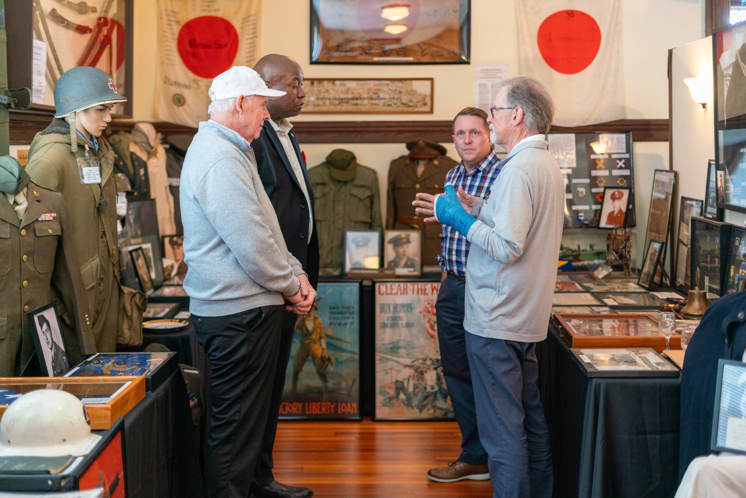 Veterans discuss military history amidst exhibits of uniforms, photographs, and memorabilia in a museum, highlighting the significance of remembrance.