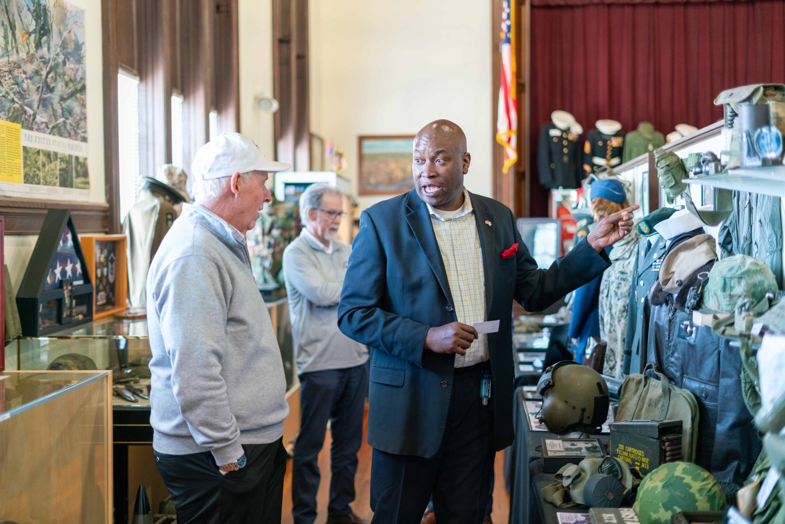 A museum guide engages visitors, discussing military artifacts displayed in a historic exhibition space, highlighting their significance.