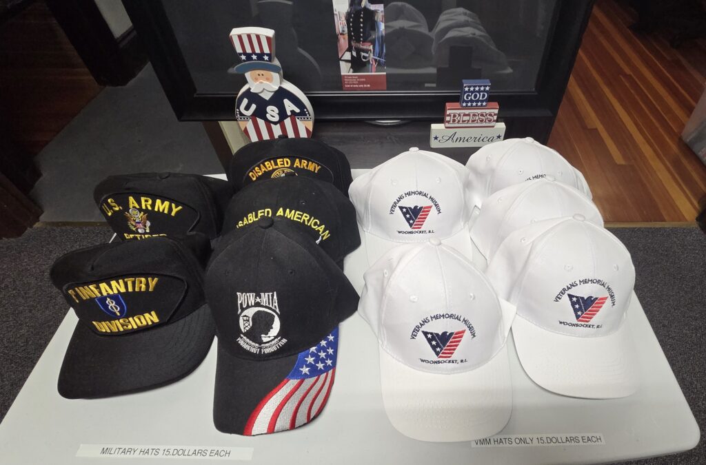 Military and veterans' hats for sale, including black hats with insignia and white hats for the Veterans Memorial Mission. Pricing displayed.